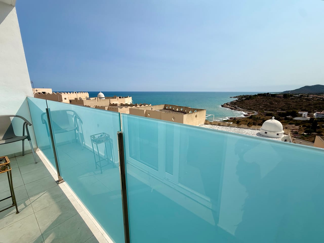 Terraza con barandilla de cristal turquesa y vistas al mar con el castillo de Peñíscola al fondo